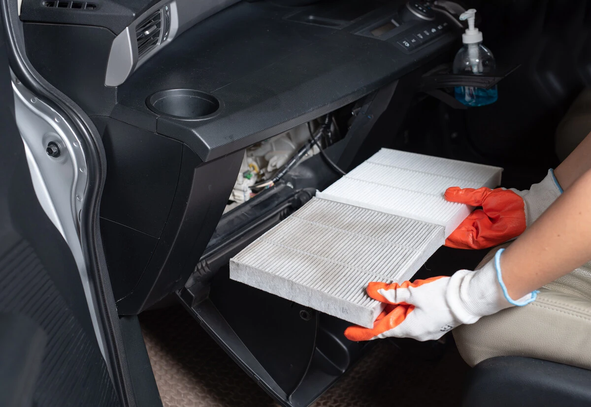 Hands in gloves changing a cabin air filter in a car